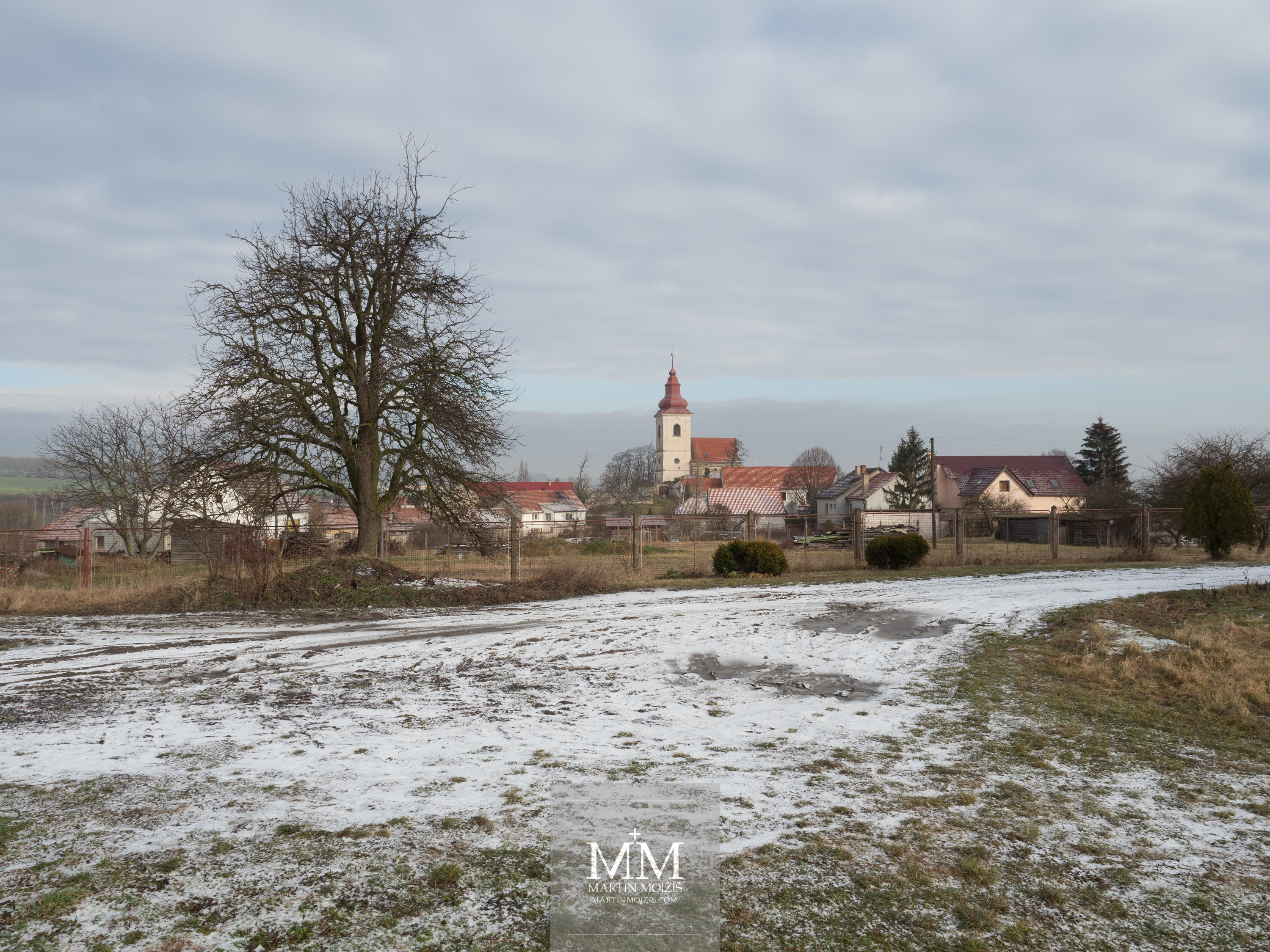 Vesnice v zimě, v pozadí kostel. Fotografie vytvořena objektivem Olympus 12 - 40 mm 2.8 Pro.